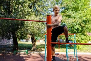 a Garoto dentro a escola parque escalou para a topo do a horizontal bar. rua exercite-se em uma horizontal Barra dentro a escola parque. foto