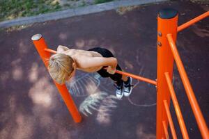 uma adolescente esticado Fora segurando para dele braços e realizando acrobático exercícios em uma horizontal bar. rua exercite-se em uma horizontal Barra dentro a escola parque. foto
