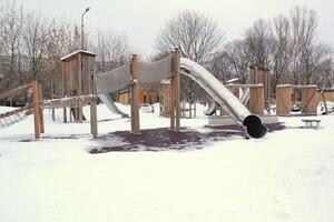 de madeira Parque infantil fez do natural ecológico material dentro público cidade parque com neve às inverno tempo. moderno segurança crianças ao ar livre equipamento. inverno Atividades. crianças descansar e jogos em aberto ar foto