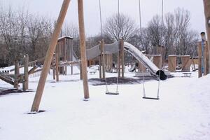 de madeira Parque infantil fez do natural ecológico material dentro público cidade parque com neve às inverno tempo. moderno segurança crianças ao ar livre equipamento. inverno Atividades. crianças descansar e jogos em aberto ar foto