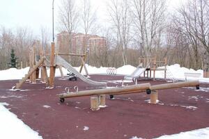 de madeira Parque infantil fez do natural ecológico material dentro público cidade parque com neve às inverno tempo. moderno segurança crianças ao ar livre equipamento. inverno Atividades. crianças descansar e jogos em aberto ar foto