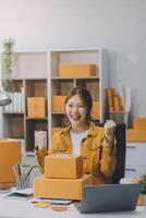 mulheres de negócios asiáticas usam laptop verificando caixas de remessa on-line de pedidos de clientes em casa. começando pequeno empresário freelance. negócio online, trabalho em casa conceito. foto