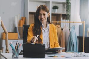 retrato lindo sorrir ásia desenhador mulher usar computador dentro alfaiate tecido moda pequeno o negócio conectados oficina. jovem proprietário comece empreendedor. criativo menina têxtil vestuário sme o negócio conceito foto