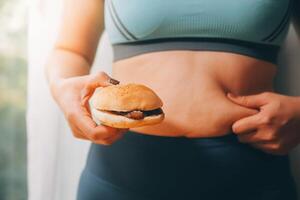 retrato do obeso mulher parece triste enquanto beliscar dela barriga gordo cercado de lixo alimentos. dieta falhou conceito foto