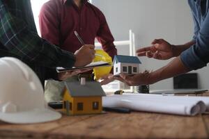 engenheiros estão consultando a equipe para Projeto a arquitetônico estrutura para clientes com plantas e construção modelos para trabalhos às escritório. foto