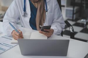 fêmea médico sentado às escrivaninha e escrevendo uma prescrição para dela paciente foto