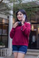 retrato do lindo sexy ásia mulher explorando cafeteria ao ar livre. sorridente menina segurando de alguém célula telefone foto