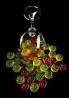 muitos pirulitos derramar Fora a partir de a derrubado vidro cálice. multicolorido doces dentro uma vidro em uma Preto fundo. foto