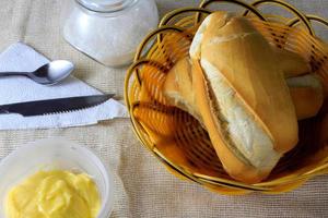 Feche o pão francês na mesa do café da manhã de madeira com manteiga e talheres foto