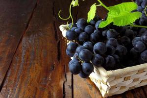 cachos de uvas, dentro de uma cesta de fibra de bambu na mesa de madeira foto