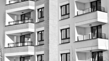 fragmento do a edifício de fachada com janelas e varandas. moderno apartamento edifícios em uma ensolarado dia. fachada do uma moderno residencial prédio. Preto e branco. foto