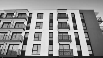 fragmento do a edifício de fachada com janelas e varandas. moderno apartamento edifícios em uma ensolarado dia. fachada do uma moderno residencial prédio. Preto e branco. foto