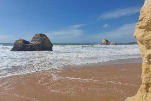 rochoso mar pilhas em arenoso de praia com ondas falhando. foto