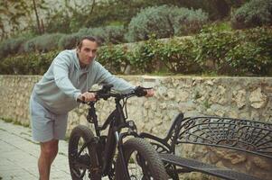 caucasiano jovem homem 40. anos velho, empurrando elétrico montanha bicicleta acima a rua. ativo estilo de vida. esporte. aventura viagem em bicicleta. usando el-bicicleta de Anúncios ecologicamente amigáveis modo do urbano transporte foto