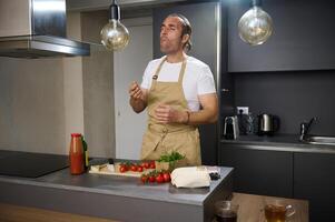 bonito hispânico jovem homem degustação ingredientes enquanto cozinhando jantar às casa cozinha, em pé às cozinha mesa com ingredientes, expressando satisfação do a gosto do legumes. pessoas. saudável Comida foto