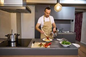 atraente bonito europeu masculino chefe de cozinha derramando tomate molho em italiano massa, chapeamento acima a prato antes servindo. homem cozinhando jantar às casa cozinha. cozinha. culinária. epicurista. Comida conceito foto