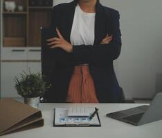 jovem feliz empresária usando computador dentro moderno escritório com colegas. à moda lindo Gerente sorridente, trabalhando em financeiro e marketing projetos. bebendo chá ou café a partir de uma caneca. foto