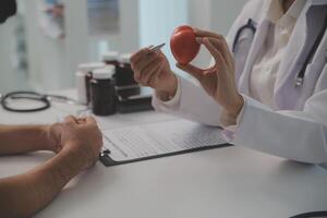 mãos do médico mulher segurando vermelho coração, mostrando símbolo do amor, humano Apoio, suporte para paciente, promovendo médico seguro, cedo checar para assistência médica, cardiologista ajuda. fechar acima do objeto foto