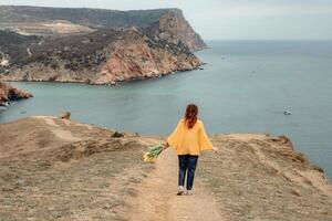 uma mulher é caminhando em uma caminho perto a oceano. ela é carregando uma ramalhete do flores foto