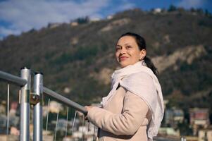 jovem mulher turista admira a lago do como a partir de a beira-mar, sobre alpino montanhas fundo, sorrisos e sonhadoramente olhando para dentro a distância. pessoas e natureza. viagem e turismo conceito. Itália foto