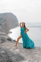 mulher mar trevel verde vestir. lado Visão uma feliz mulher com grandes cabelo dentro uma grandes hortelã vestir posando em uma de praia com calma mar bokeh luzes em ensolarado dia. menina em a natureza em azul céu fundo. foto