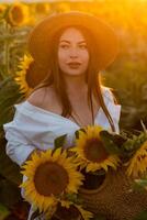 uma menina dentro uma chapéu em uma lindo campo do girassóis contra a céu dentro a tarde luz do uma verão pôr do sol. raios solares através a flor campo. natural fundo. foto