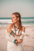 modelo dentro boho estilo dentro uma branco grandes vestir e prata joalheria em a de praia. dela cabelo é trançado, e lá estão muitos pulseiras em dela braços. foto