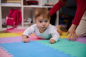 seletivo foco em adorável bebê Garoto rastejando em a colorida enigma tapete com a Socorro do dele jovem amoroso carinhoso irmã. crianças crescimento e desenvolvimento. infância. infância. família foto