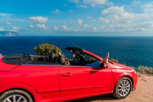 uma mulher é deitado em dela pés dentro uma vermelho carro, olhando Fora a janela às a oceano foto