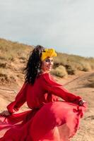uma mulher dentro uma vermelho vestir e amarelo arco de cabelo é caminhando em uma sujeira caminho. ela é sorridente e ela é feliz. foto