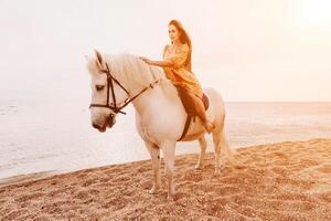 uma mulher dentro uma vestir carrinhos Próximo para uma branco cavalo em uma praia, com a azul céu e mar dentro a fundo. foto