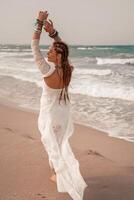 modelo dentro boho estilo dentro uma branco grandes vestir e prata joalheria em a de praia. dela cabelo é trançado, e lá estão muitos pulseiras em dela braços. foto