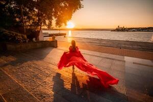 nascer do sol vermelho vestir. uma mulher dentro uma grandes vermelho vestir contra a pano de fundo do nascer do sol, brilhante dourado luz do a do sol raios. a conceito do feminilidade, harmonia. foto