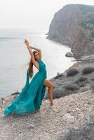 mulher mar verde vestir. lado Visão uma feliz mulher com grandes cabelo dentro uma grandes hortelã vestir posando em uma de praia com calma mar bokeh luzes em ensolarado dia. menina em a natureza em azul céu fundo. foto