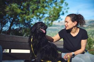 feliz mulher e Preto Cocker spaniel cachorro em a Banco dentro a montanhas. pessoas e animais. jogando animais de estimação e animais de estimação conceito foto