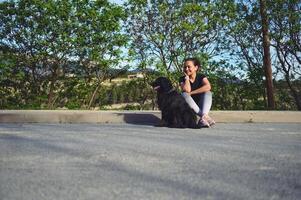 cheio Tamanho retrato do mulher sentado em a parapeito e falando para dela cachorro enquanto levando dela animal para uma andar em a natureza foto