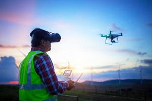 engenheiro operar drone voando para fazenda eólica de construção de pesquisa no pôr do sol. foto