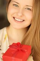 feliz sorridente mulher segurando uma vermelho presente caixa, face retrato com natural Maquiagem e feriado estilo de vida às casa foto