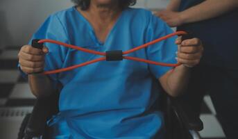 pessoal treinador ajudando Senior mulher com resistência banda. reabilitação fisioterapia trabalhador ajudando velho paciente às enfermagem lar. velho mulher com esticam banda ser treinado de fisioterapeuta. foto