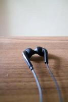 uma par do fones de ouvido com cabos. preto, colocada em uma mesa com uma de madeira motivo foto