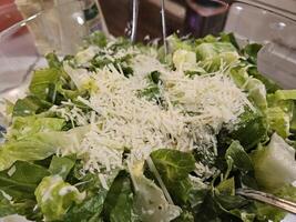 cesar salada com cesar vestir servido com parmesão queijo dentro uma grande tigela preenchidas com alface foto