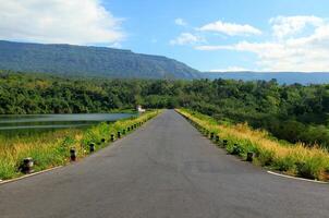 a estrada alongar ao longo uma lindo rio ou lago, com montanhas, azul céu, branco nuvem e verde florestas dentro a primeiro plano às wang bom reservatório, Nakhon nayok, tailândia. foto