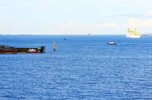 Porto e barco estão carregando carga em a mar dentro Cingapura. transporte e lindo panorama Visão do oceano com Claro azul céu e nuvem fundo. foto