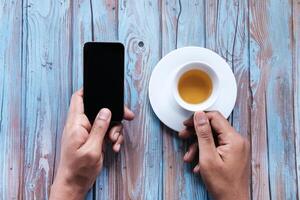 do homem mãos segurando Móvel telefone com em branco tela e uma café copo. foto