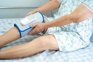 paciente asiático sênior ou idosa com massagem nas pernas de pressão de compressão de ar sem fio na cama em um hospital de enfermagem.