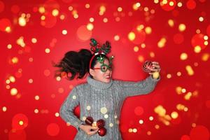 Natal ano novo. jovem vestida com uma camisola quente com adereços bola vermelha com enfeites de Natal em férias em fundo vermelho brilho. conceito, feliz Natal. foto