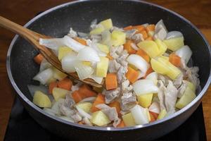 Carne de porco frita com legumes em uma panela quente. foto