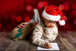 adorável garotinha usando chapéu de papai noel escrevendo carta de papai noel