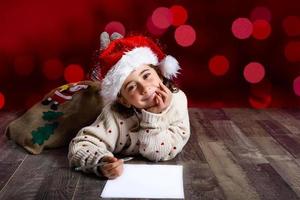 adorável garotinha usando chapéu de papai noel escrevendo carta de papai noel foto