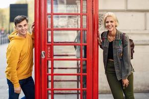 jovem casal de amigos perto de uma cabine telefônica vermelha britânica clássica foto